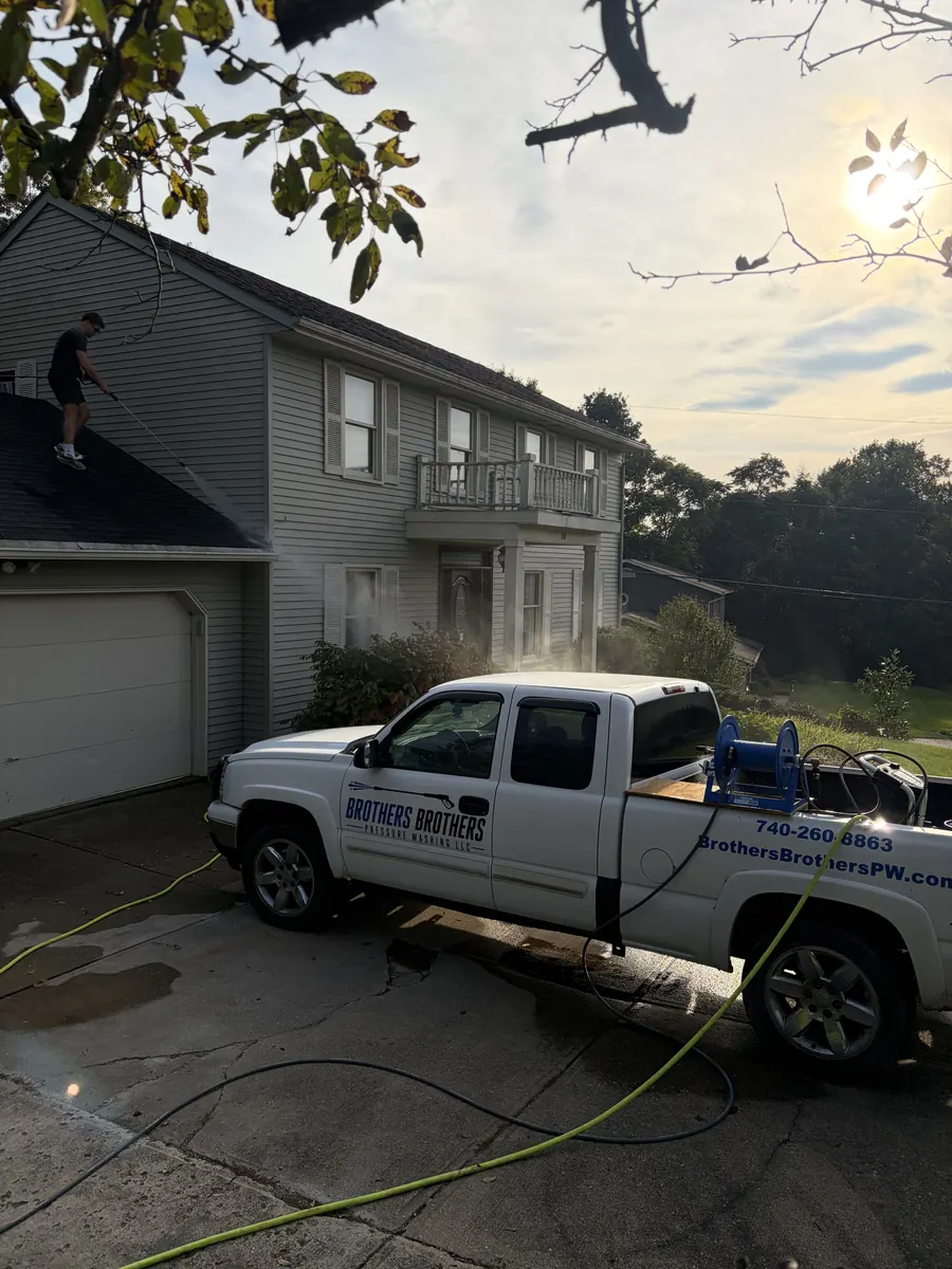 Brothers Brothers truck with hose reel in the driveway while washing a two-story house