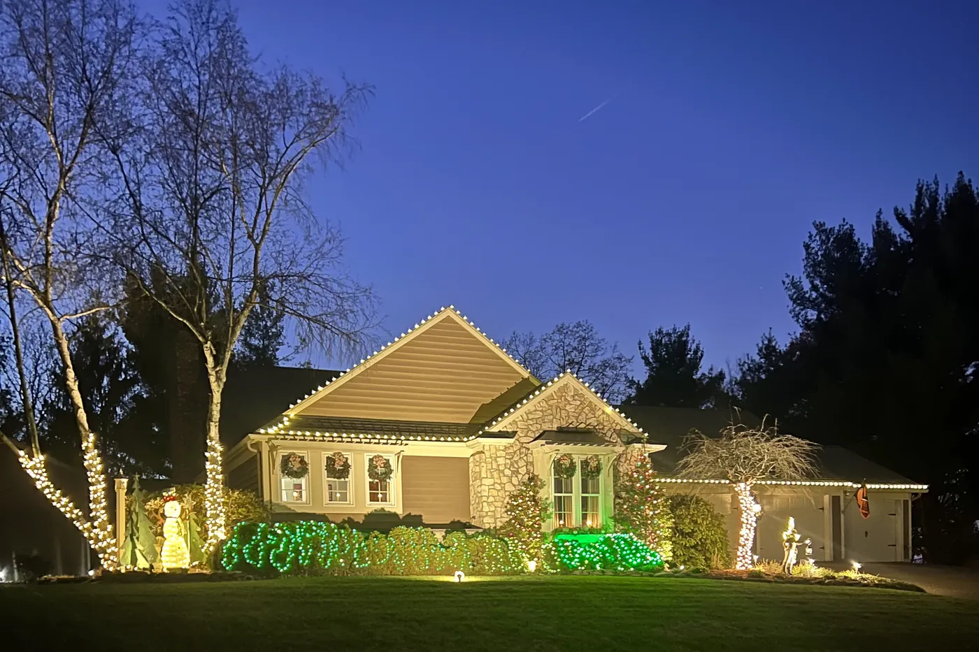 House with rooflines, bushes and trees lit up with Christmas lights